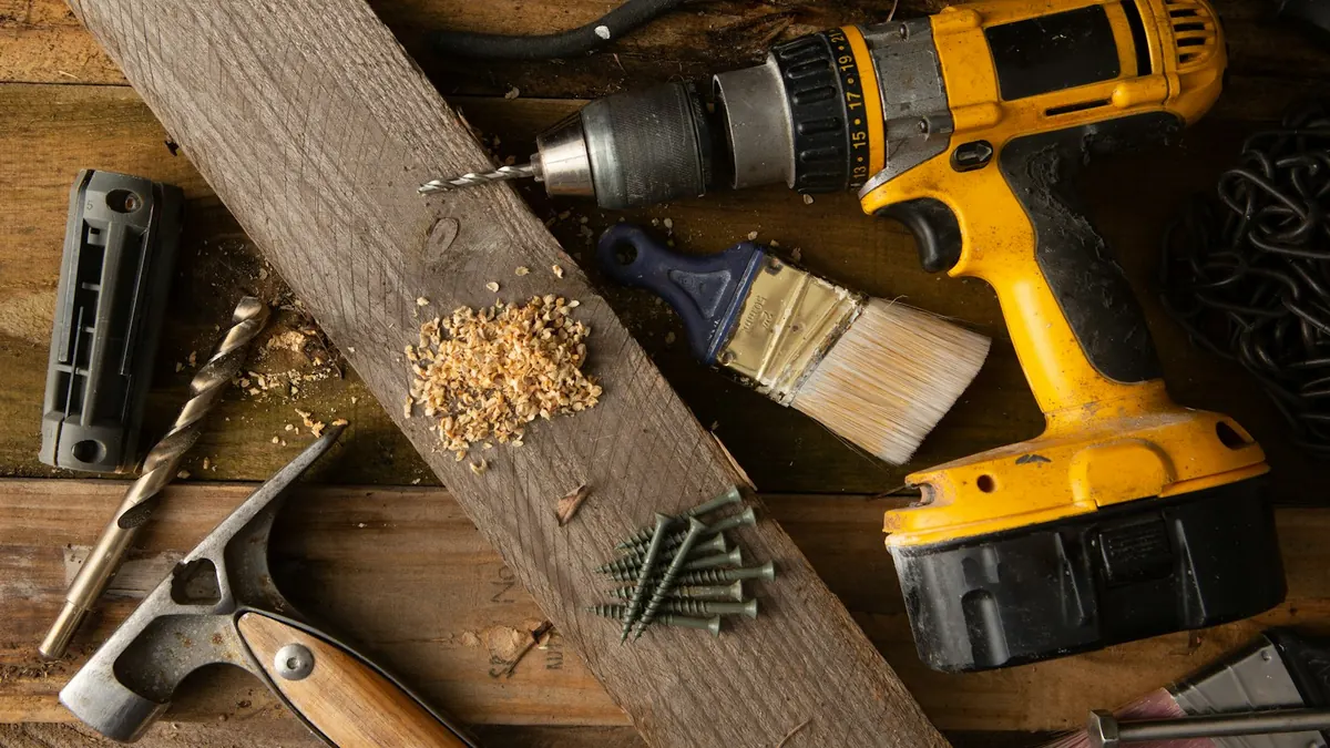 Outils de montage posés sur une pièce de bois : perceuse, visserie, crayon