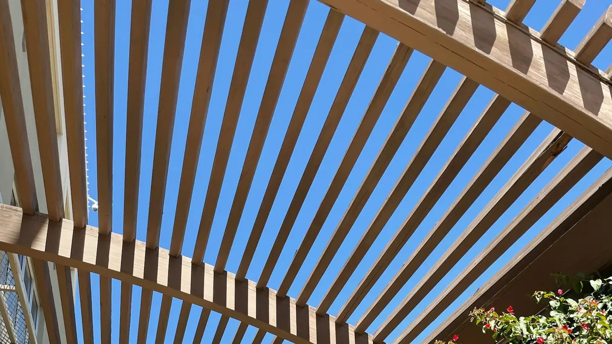 Lames en bois d'une pergola et leurs ombres portées sur une terrasse